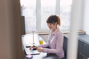 Smiling businesswoman using credit card in office - PNAF05263