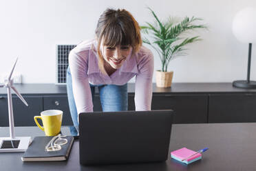 Happy businesswoman working on laptop in office - PNAF05264