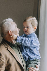 Grandfather carrying grandson at home - VSNF00703