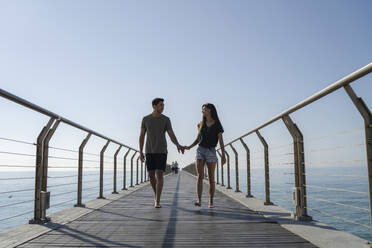 Young couple walking on bridge under sky - IKF00135