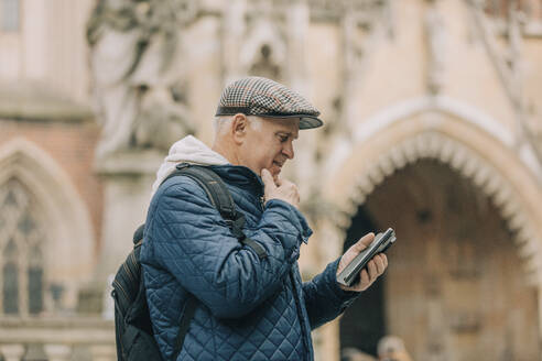 Älterer Mann mit Smartphone vor einer Kathedrale stehend - VSNF00706