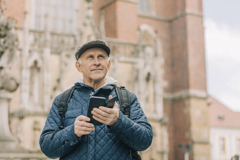 Älterer Mann mit Smartphone vor einer Kathedrale stehend - VSNF00708