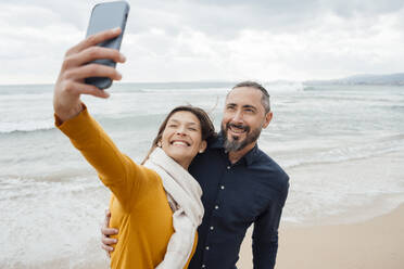 Ein fröhliches Paar hält einen Moment der Zweisamkeit fest, indem es mit seinem Handy ein Selfie am Strand macht - JOSEF18491