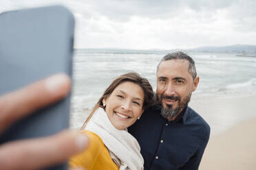 Eine fröhliche Frau fängt einen Moment mit einem älteren Mann am Strand ein, indem sie ihr Mobiltelefon für ein Selfie benutzt - JOSEF18492