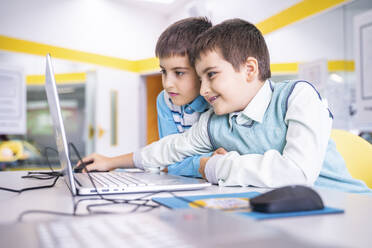 Lächelnder Junge, der sich einen Laptop mit einem Freund im Computerkurs in der Schule teilt - NJAF00341
