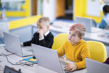 Junge träumt mit Laptop im Unterricht in der Schule - NJAF00344