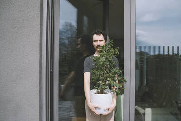 Man holding potted plant standing by glass door - NDEF00536