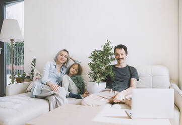 Lächelnder Mann und Frau sitzen mit ihrem Sohn zu Hause auf dem Sofa - NDEF00537