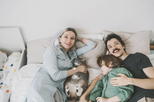 Happy family with cat relaxing on bed at home - NDEF00542