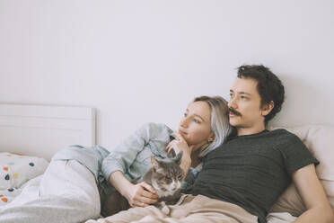 Thoughtful couple with cat lying on bed at home - NDEF00548