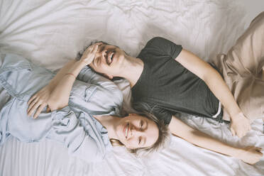 Smiling woman touching forehead of man lying on bed at home - NDEF00555