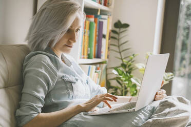 Frau benutzt Laptop auf Sofa zu Hause - NDEF00568