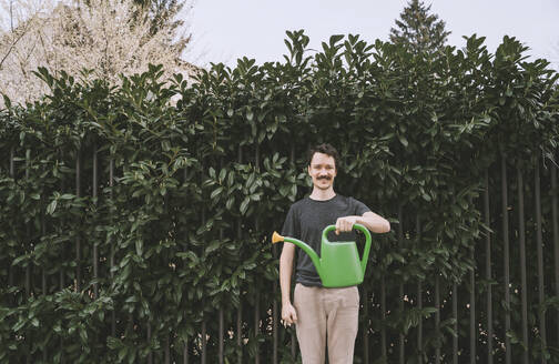 Smiling man standing with watering can in front of plants - NDEF00569