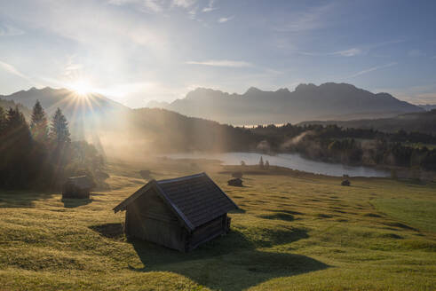 Deutschland, Bayern, Einsam gelegene Hütten im Karwendelgebirge bei nebligem Sonnenaufgang mit Geroldsee im Hintergrund - RUEF04033