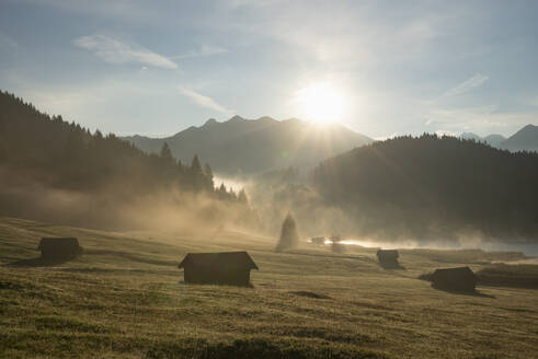 Deutschland, Bayern, Einsam gelegene Hütten im Karwendelgebirge bei nebligem Sonnenaufgang mit Geroldsee im Hintergrund - RUEF04034