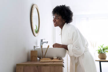 Woman wearing bathrobe looking in mirror at home - AAZF00302