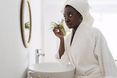 Frau im Bademantel mit Jadewalze auf dem Gesicht im Badezimmer zu Hause - AAZF00311