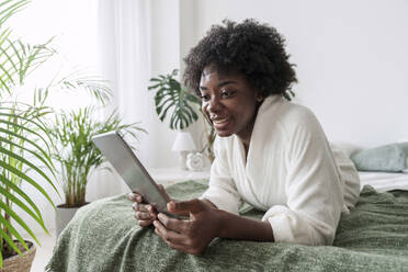 Lächelnde Frau mit Tablet-PC auf dem Bett liegend zu Hause - AAZF00330