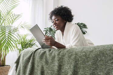 Frau mit Tablet-Computer auf dem Bett liegend zu Hause - AAZF00332