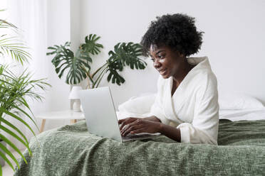 Frau mit Laptop auf dem Bett liegend zu Hause - AAZF00333