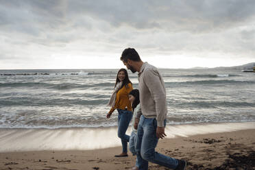 Happy woman and man walking with daughter at beach - JOSEF18504