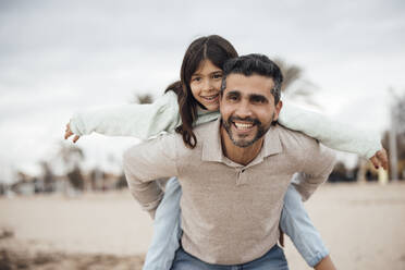 Smiling man giving piggyback ride to daughter at beach - JOSEF18508