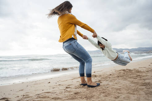Woman spinning daughter and having fun at beach - JOSEF18528