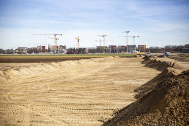 Deutschland, Bayern, München, Sandige Fläche für Baustelle vorbereitet mit Industriekränen im Hintergrund - MAMF02840