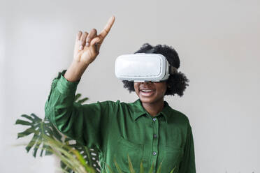 Smiling woman pointing finger and wearing virtual reality simulator - AAZF00367