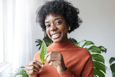 Smiling young woman with leaf at home - AAZF00390