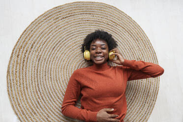 Happy young woman lying on rug and listening to music - AAZF00393