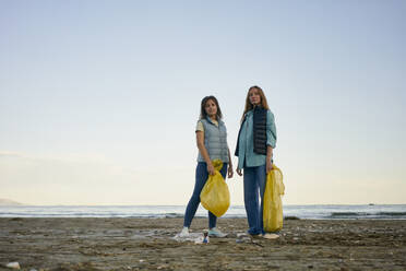 Aktivistische Frauen stehen am Strand und halten Plastiktüten - ANNF00101