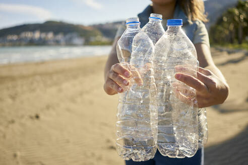 Activist holding empty plastic bottles at beach - ANNF00105