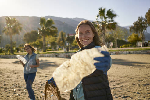 Smiling volunteer holding empty plastic bottle at beach - ANNF00114