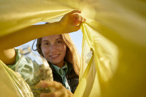 Smiling woman looking inside yellow garbage bag - ANNF00124