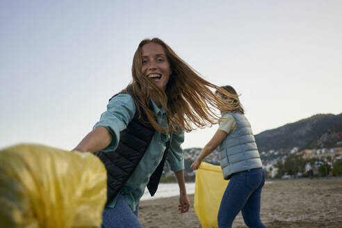 Cheerful volunteers having fun holding garbage bags at beach - ANNF00132