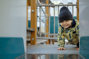 Lächelnder süßer Junge auf dem Spielplatz krabbelnd - ANAF01235