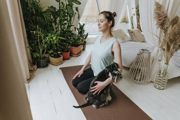 Woman practicing meditation with Schnauzer dog on exercise mat at home - YTF00740