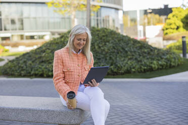Ältere Geschäftsfrau führt einen Videoanruf mit Tablet-PC auf einer Bank sitzend - JCCMF10302