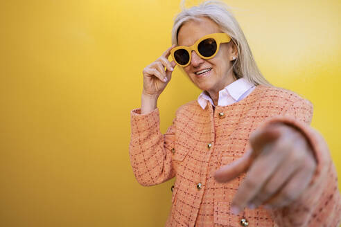 Smiling woman wearing sunglasses in front of yellow wall - JCCMF10308