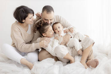 Happy family enjoying together sitting in front of white wall - GMLF01398