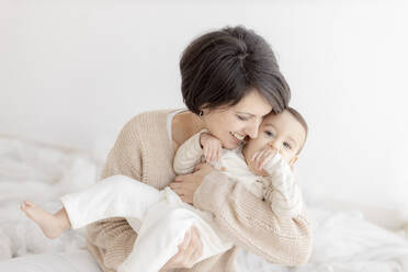 Happy mother embracing cute son in front of white wall - GMLF01402