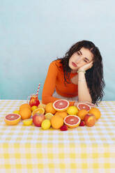 Young woman leaning on elbow with citrus fruits on table - EGHF00751