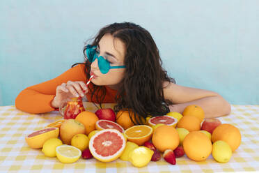 Frau mit Sonnenbrille trinkt ein Zitrusgetränk mit Früchten auf dem Tisch - EGHF00758