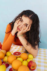 Junge Frau berührt Gesicht mit Zitrusfrüchten auf dem Tisch - EGHF00759