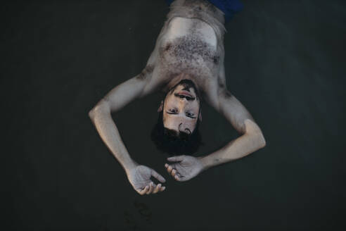 Hemdloser Mann mit erhobenen Armen schwimmt im Meer - GMLF01409