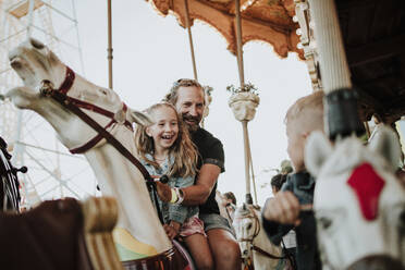 Glückliches Mädchen genießt Karussellfahrt mit Vater im Vergnügungspark - GMLF01413