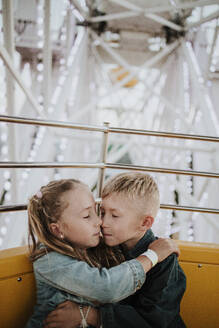 Junge und Mädchen mit geschlossenen Augen sitzen im Riesenrad im Vergnügungspark - GMLF01416