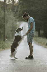 Young man standing with dog on road at sunset - GMLF01423