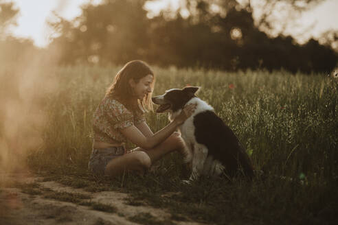 Lächelnde Frau mit Border Collie Hund auf einem Feld sitzend - GMLF01426